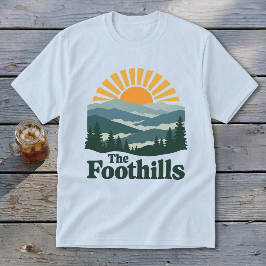 Light blue t-shirt with sunset over mountains and "The Foothills" text.
