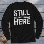Black long sleeve shirt with white "STILL HERE" text and a wavy line graphic.