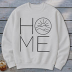 Off-white crewneck sweatshirt featuring a black graphic with the word HOME, where the letter O is replaced by mountains and a sun.