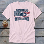 Light pink t-shirt featuring a distressed American flag graphic with the text North Carolina Raised American Made.