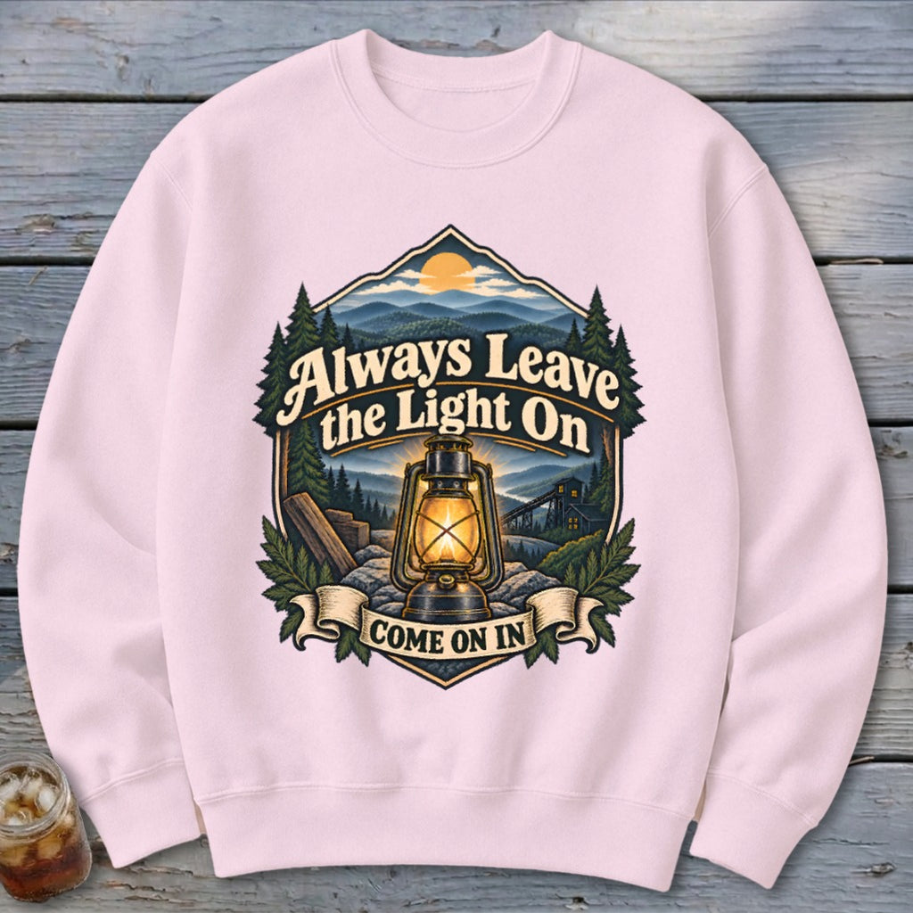 Pink sweatshirt with vintage lantern and mountain scene graphic saying "Always Leave the Light On".