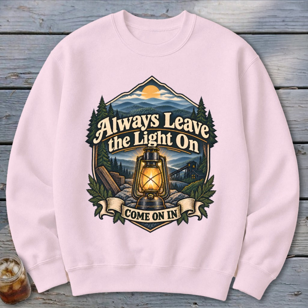 Pink sweatshirt with vintage lantern and mountain scene graphic saying "Always Leave the Light On".