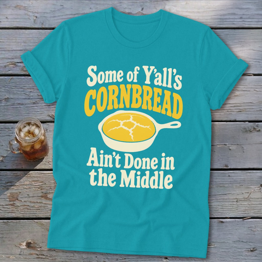 Turquoise t-shirt with rolled sleeves displaying text and a cornbread graphic on a rustic wooden background.