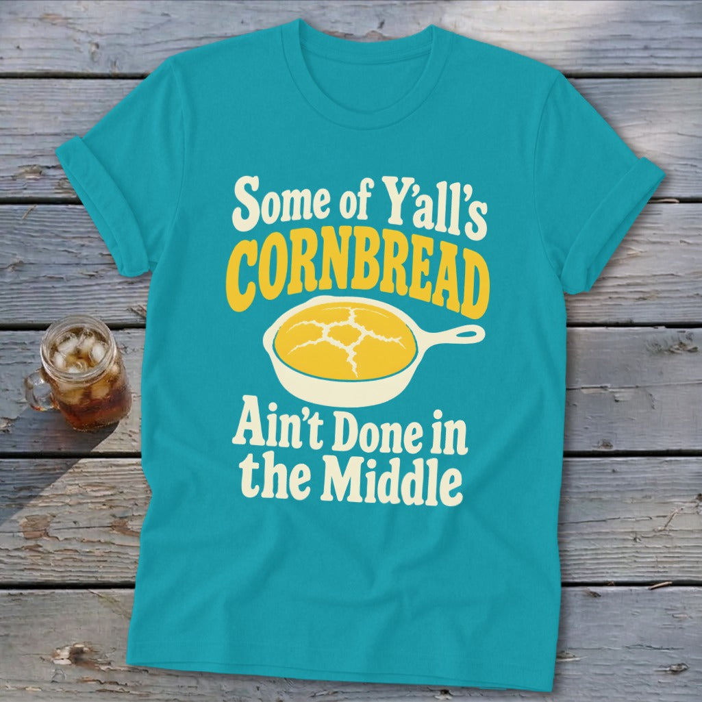 Turquoise t-shirt with rolled sleeves displaying text and a cornbread graphic on a rustic wooden background.