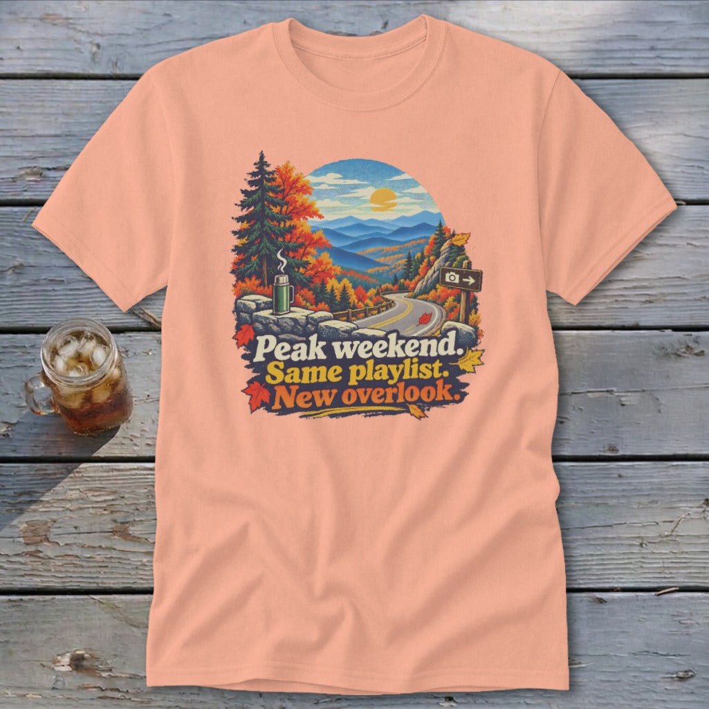 Peach t-shirt with autumn mountain road scene and text "Peak weekend. Same playlist. New overlook."