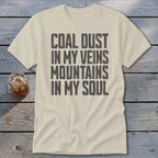 Cream-colored crewneck t-shirt with charcoal text reading "COAL DUST IN MY VEINS MOUNTAINS IN MY SOUL".