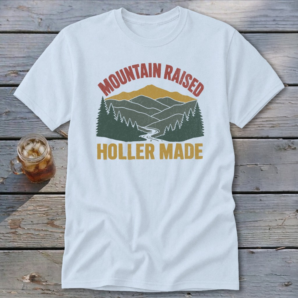 A white t-shirt featuring a retro mountain graphic with the text Mountain Raised Holler Made.