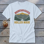 A white t-shirt featuring a retro mountain graphic with the text Mountain Raised Holler Made.