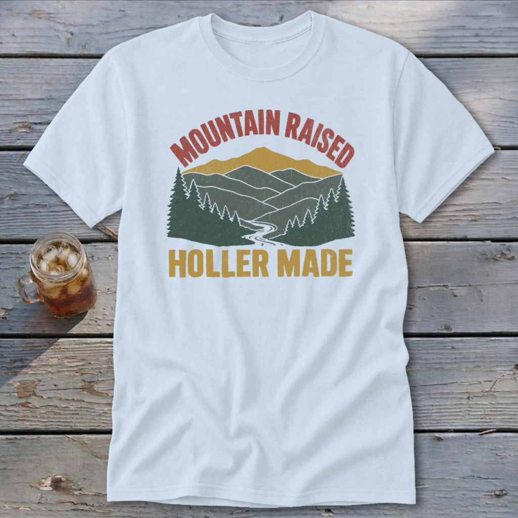 A white t-shirt featuring a retro mountain graphic with the text Mountain Raised Holler Made.