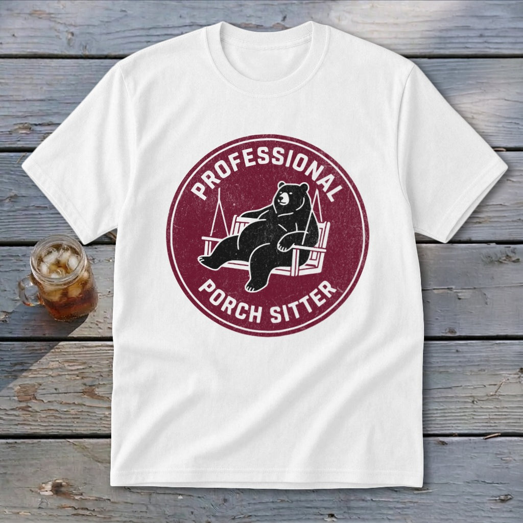 A white t-shirt featuring a circular maroon logo with a bear relaxing on a porch swing and the text PROFESSIONAL PORCH SITTER.