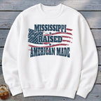 A white crewneck sweatshirt features a distressed American flag graphic with the text MISSISSIPPI RAISED AMERICAN MADE.