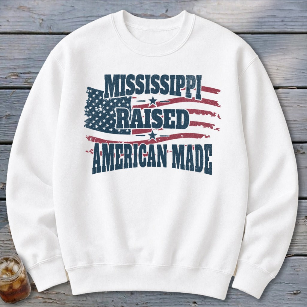 A white crewneck sweatshirt features a distressed American flag graphic with the text MISSISSIPPI RAISED AMERICAN MADE.