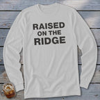 White long-sleeved shirt with "RAISED ON THE RIDGE" printed in black.