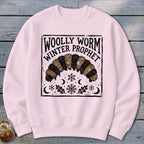 A light pink crewneck sweatshirt features a black-and-beige block print of a woolly worm and snowflakes.