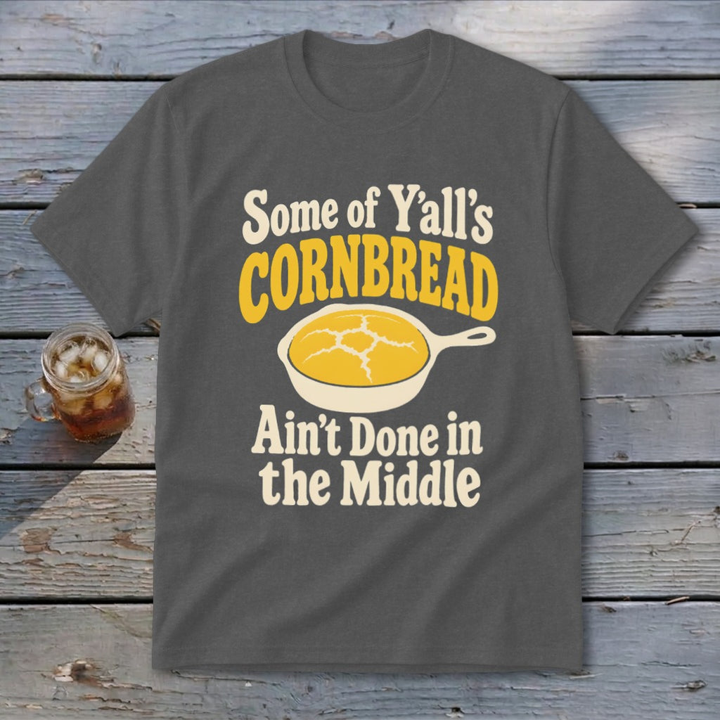 Dark gray t-shirt with cream and yellow text reading Some of Y'all's Cornbread Ain't Done in the Middle above a skillet of cornbread.