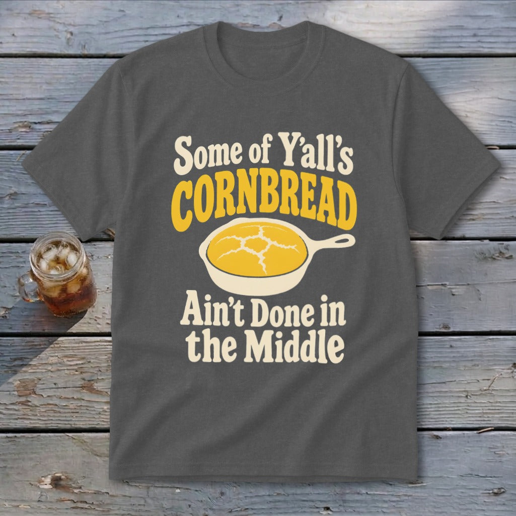 Dark gray t-shirt with cream and yellow text reading Some of Y'all's Cornbread Ain't Done in the Middle above a skillet of cornbread.