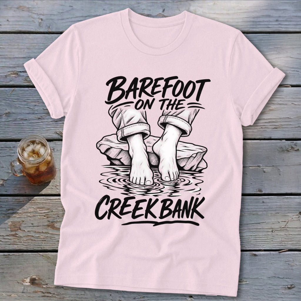 Pink t-shirt with graphic of bare feet on rocks in water, "Barefoot on the Creek Bank" text.