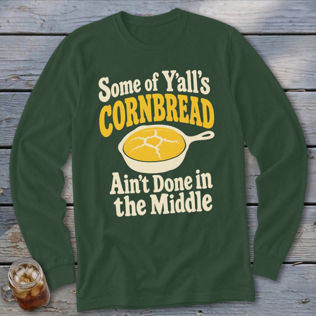 Dark green long-sleeve t-shirt with text reading Some of Y'all's Cornbread Ain't Done in the Middle and a graphic of cornbread in a skillet.