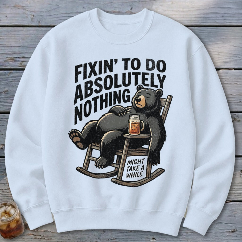 White crewneck sweatshirt featuring a cartoon black bear relaxing in a rocking chair with a drink.
