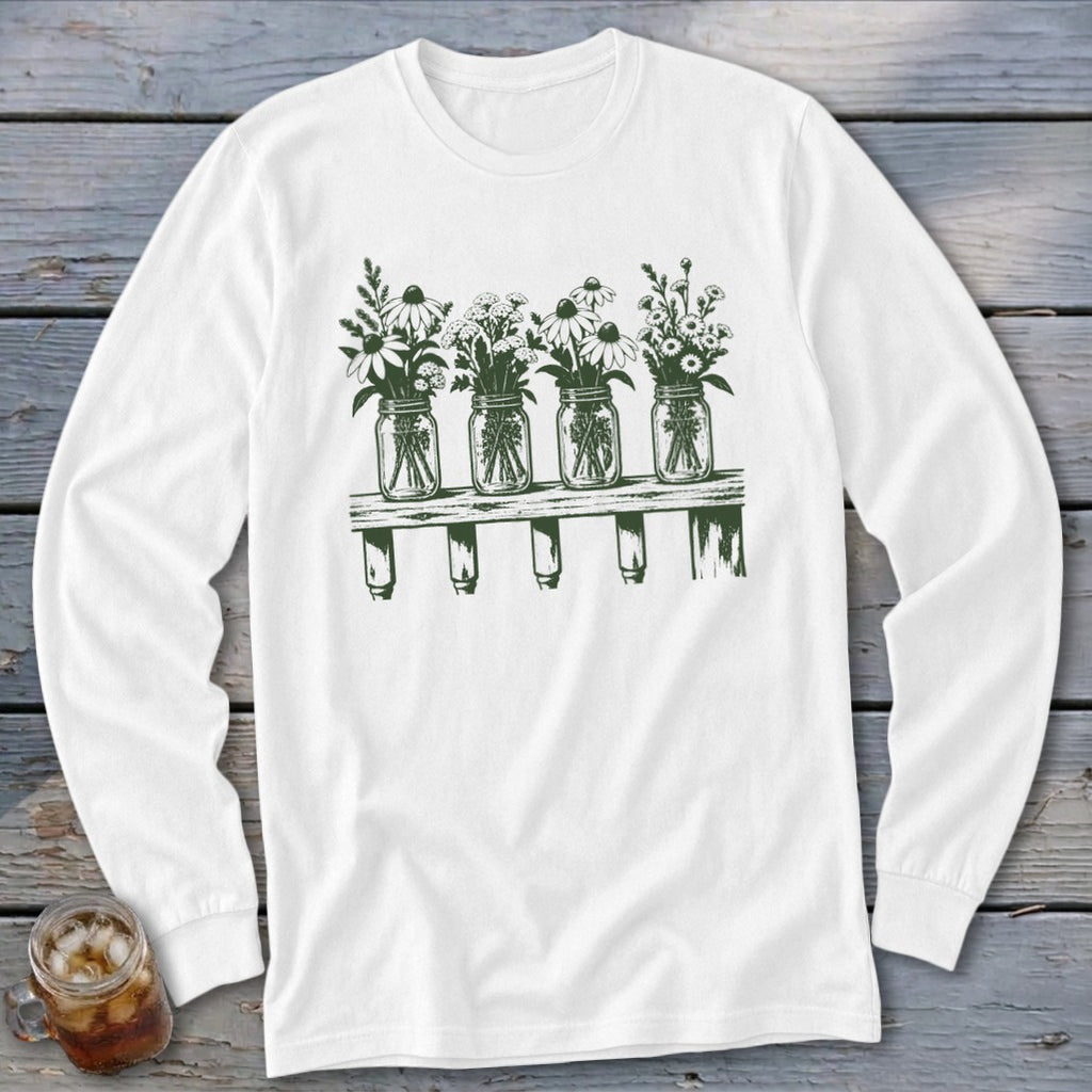 A white long-sleeved t-shirt featuring a green graphic of four mason jars filled with wildflowers on a wooden shelf.