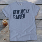 Light blue t-shirt with dark blue text "Kentucky Raised" and a glass of iced tea.