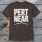 A dark brown t-shirt featuring the white text PERT NEAR and a mountain range graphic underneath.