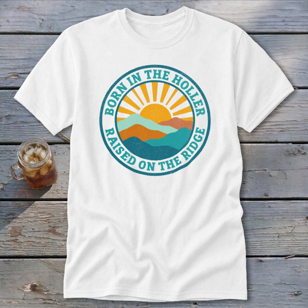 A white short-sleeved t-shirt featuring a retro mountain and sunrise graphic with the text Born in the Holler Raised on the Ridge.