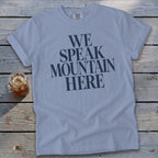 Light blue t-shirt with "WE SPEAK MOUNTAIN HERE" graphic and a drink.