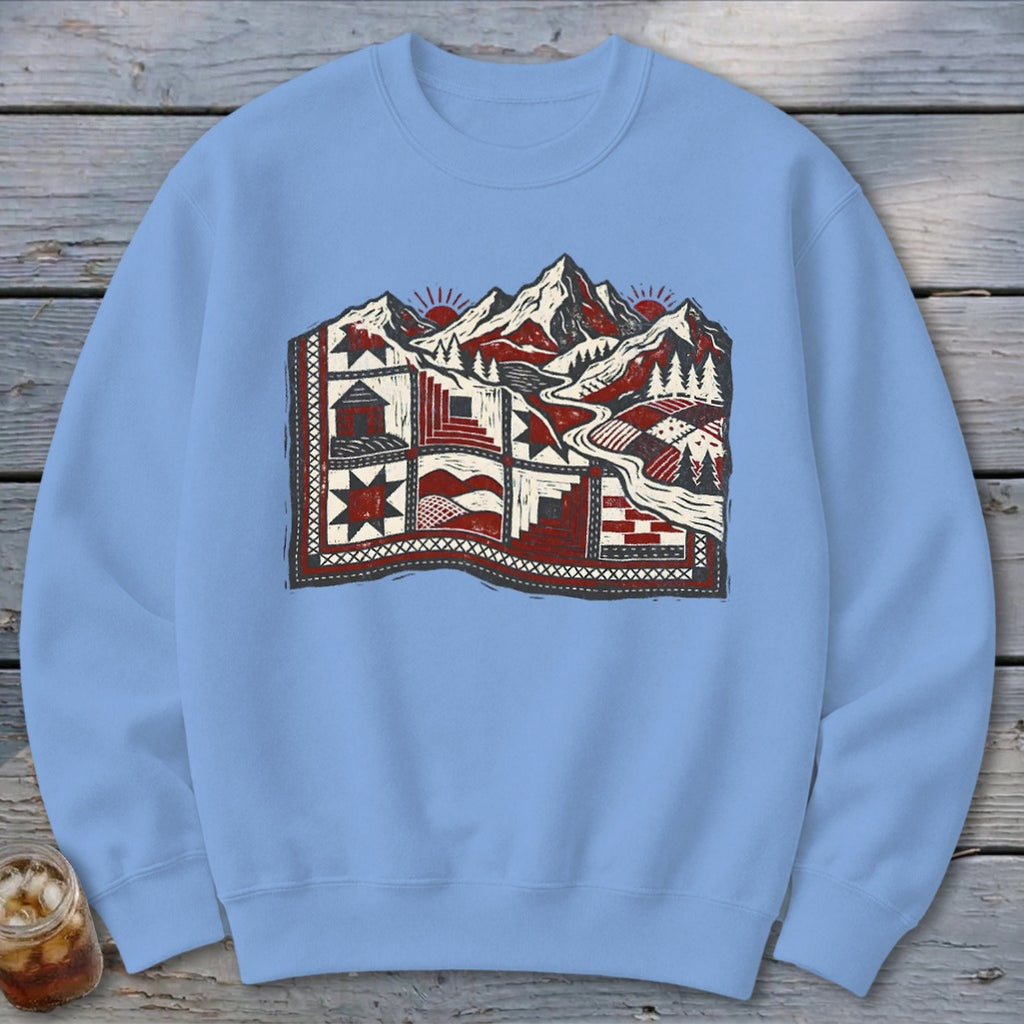 Light blue crewneck sweatshirt featuring a graphic of a patchwork quilt merging into a mountain landscape.