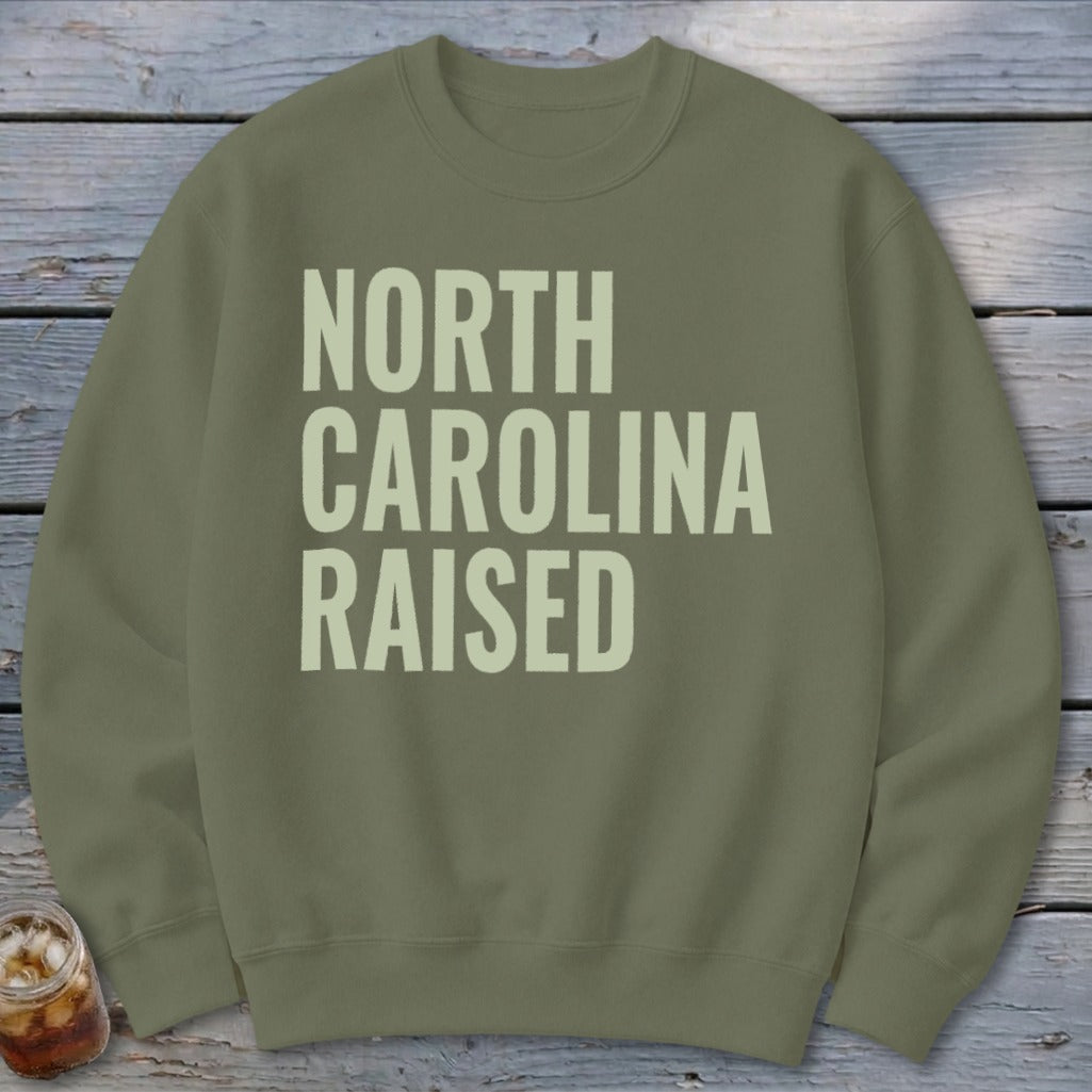 Olive green sweatshirt with "North Carolina Raised" text in light cream.