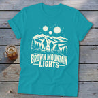 Teal crewneck t-shirt featuring a graphic of three figures looking at glowing lights above mountains.