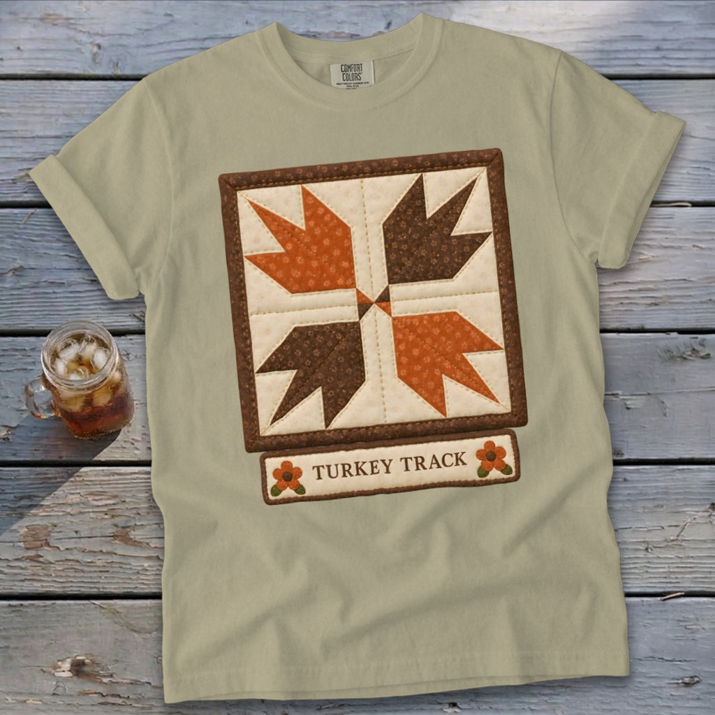 Light tan t-shirt with a quilted "Turkey Track" design and small floral accents.