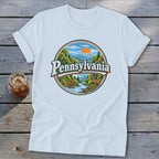 White t-shirt with Pennsylvania circular nature graphic featuring mountains, river, deer, and sun.