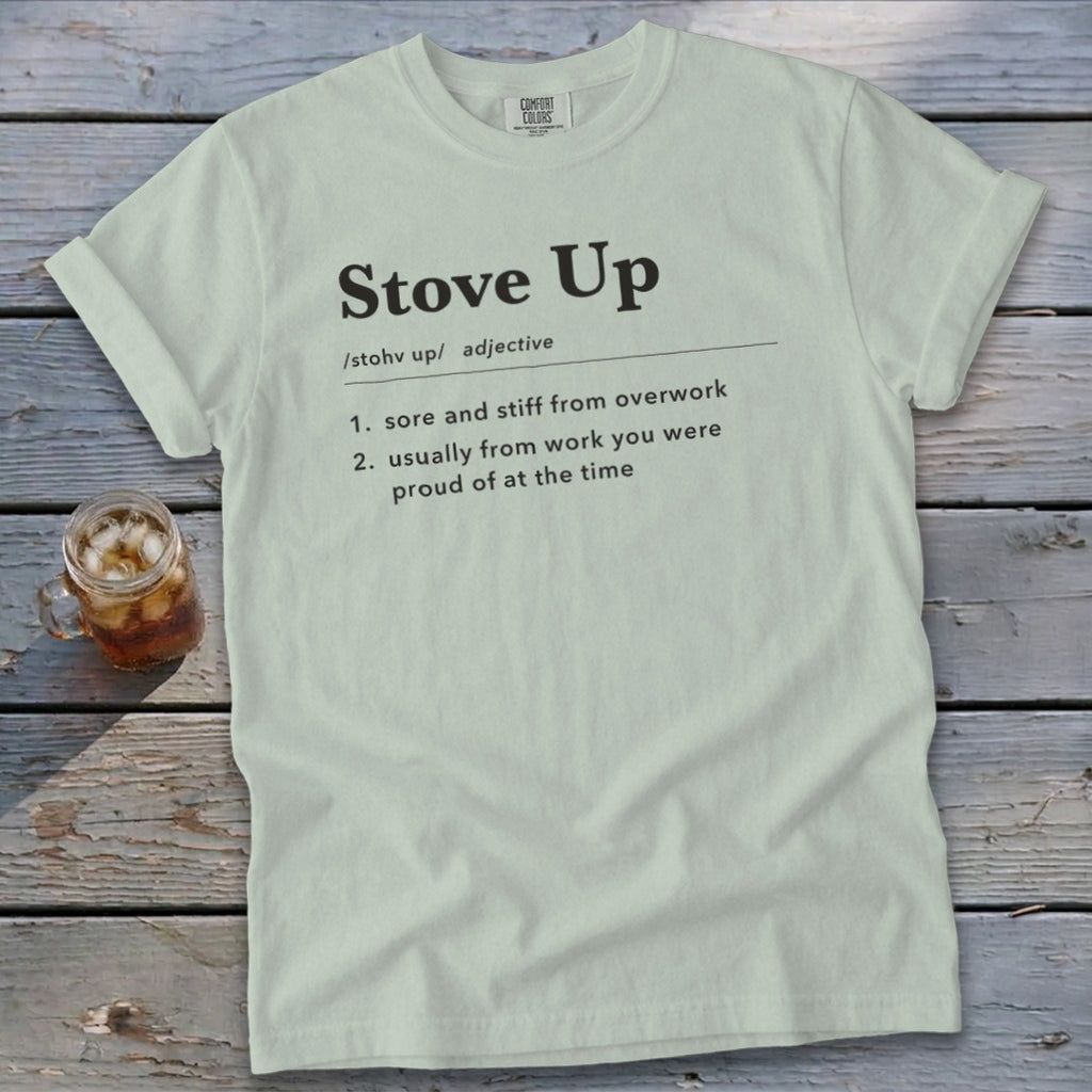A light green t-shirt with the definition of stove up printed on the front, resting on weathered wood.