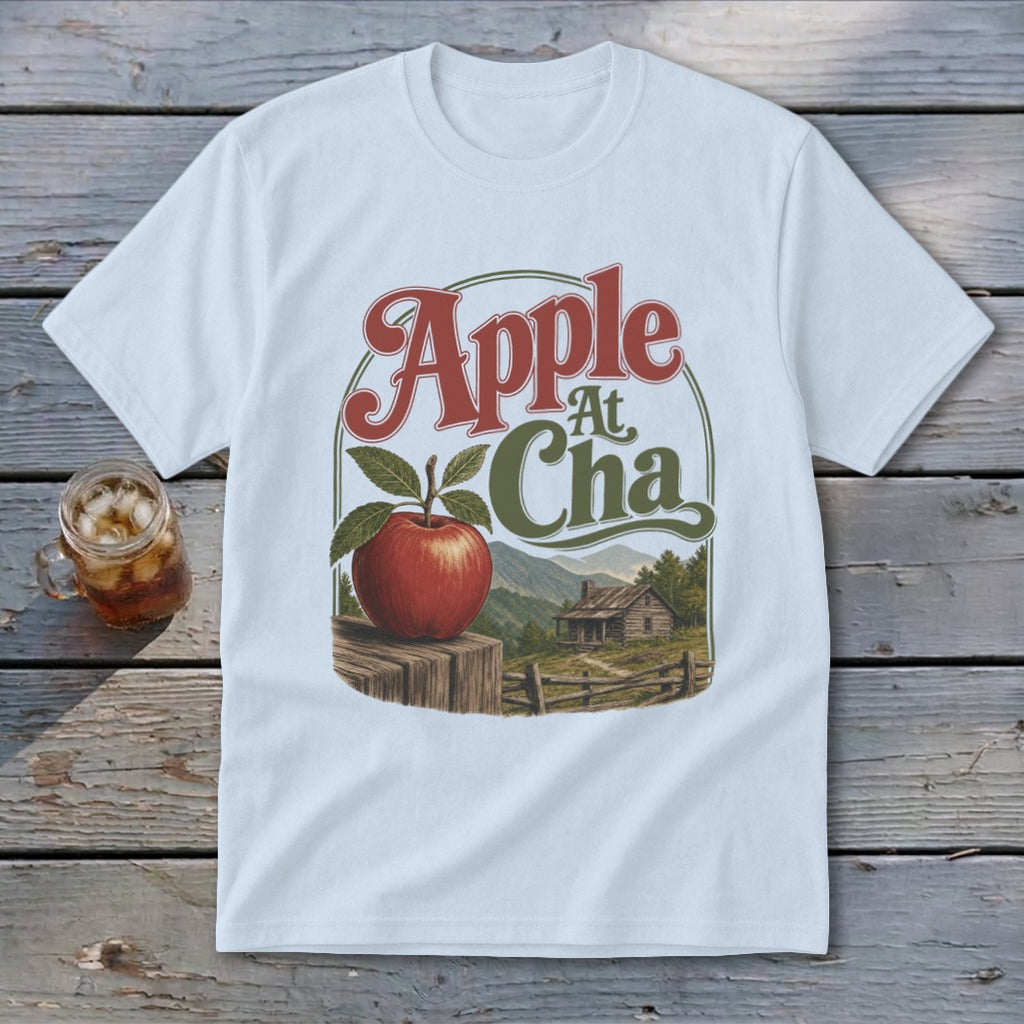 A light blue t-shirt printed with a vintage graphic of an apple, cabin, and mountains, labeled Apple At Cha.