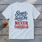 A white t-shirt with red and blue text reading Sugar in my Sweet Tea NEVER IN MY CORNBREAD on a wooden background.