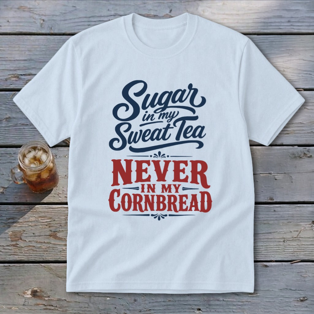A white t-shirt with red and blue text reading Sugar in my Sweet Tea NEVER IN MY CORNBREAD on a wooden background.