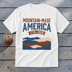 White short-sleeved t-shirt with Mountain-Made America 1776-2026 text and distressed mountain graphics in red, white, and blue.