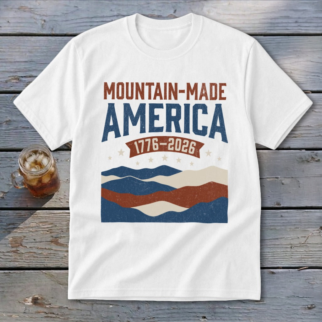 White short-sleeved t-shirt with Mountain-Made America 1776-2026 text and distressed mountain graphics in red, white, and blue.
