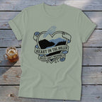 Green t-shirt with heart design featuring a bird and mountains, text reads "Heart in the Holler Miles Can't Measure It".
