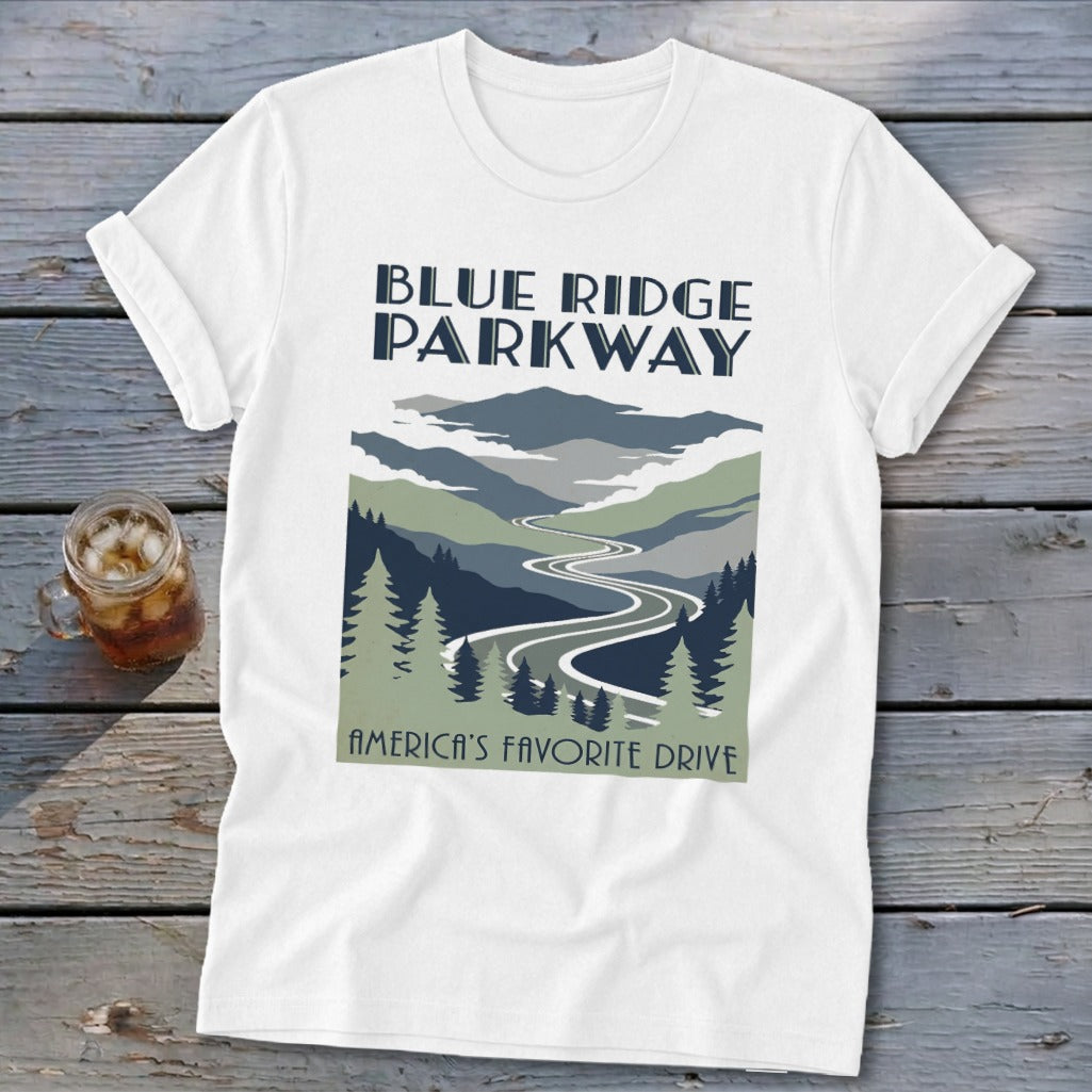 A white short-sleeved t-shirt features a Blue Ridge Parkway graphic with mountains, a winding road, and evergreen trees.