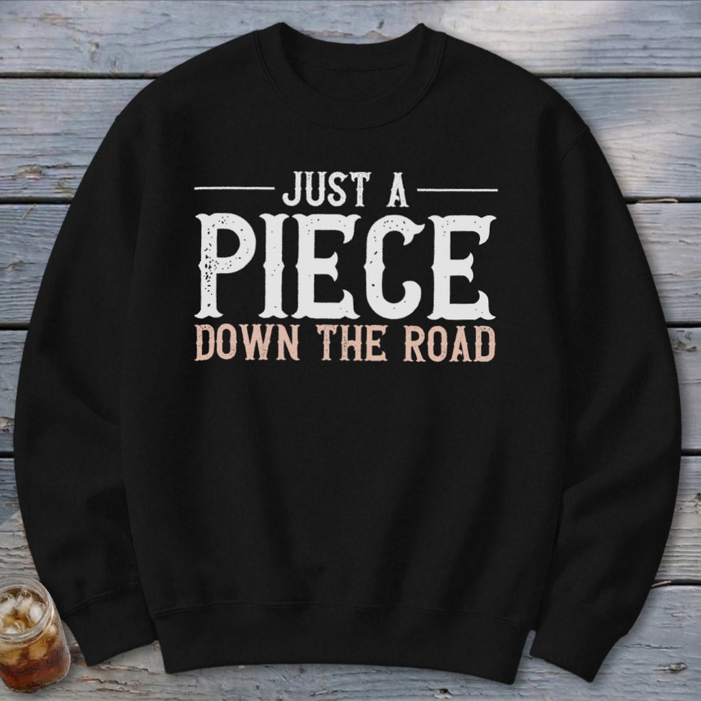 Black sweatshirt with white text reading "JUST A PIECE DOWN THE ROAD."