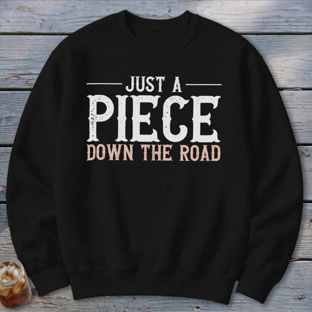 Black sweatshirt with white text reading "JUST A PIECE DOWN THE ROAD."