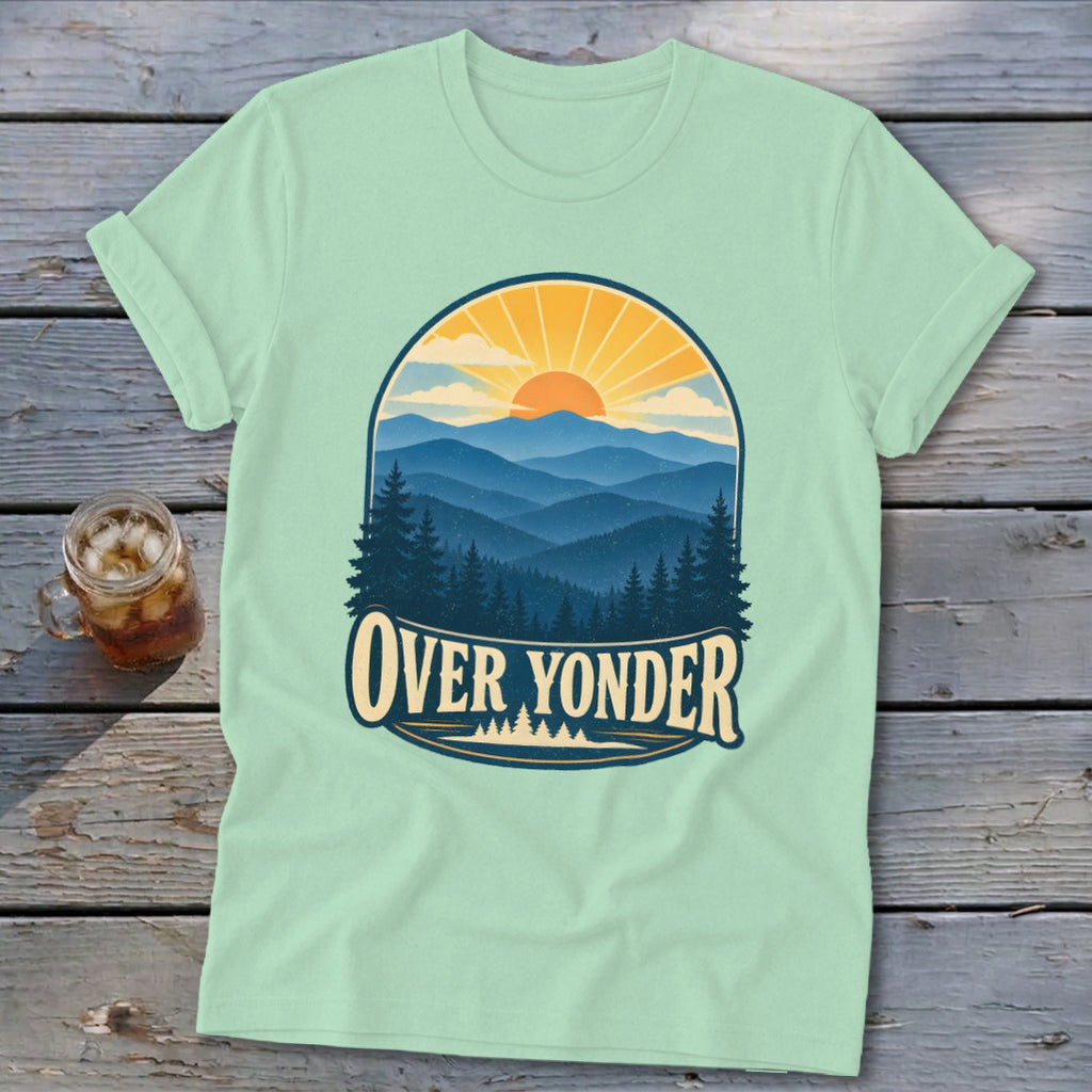 Light green t-shirt with a vintage mountain landscape graphic and the text Over Yonder on a wooden background.