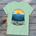 Light green t-shirt with a vintage mountain landscape graphic and the text Over Yonder on a wooden background.
