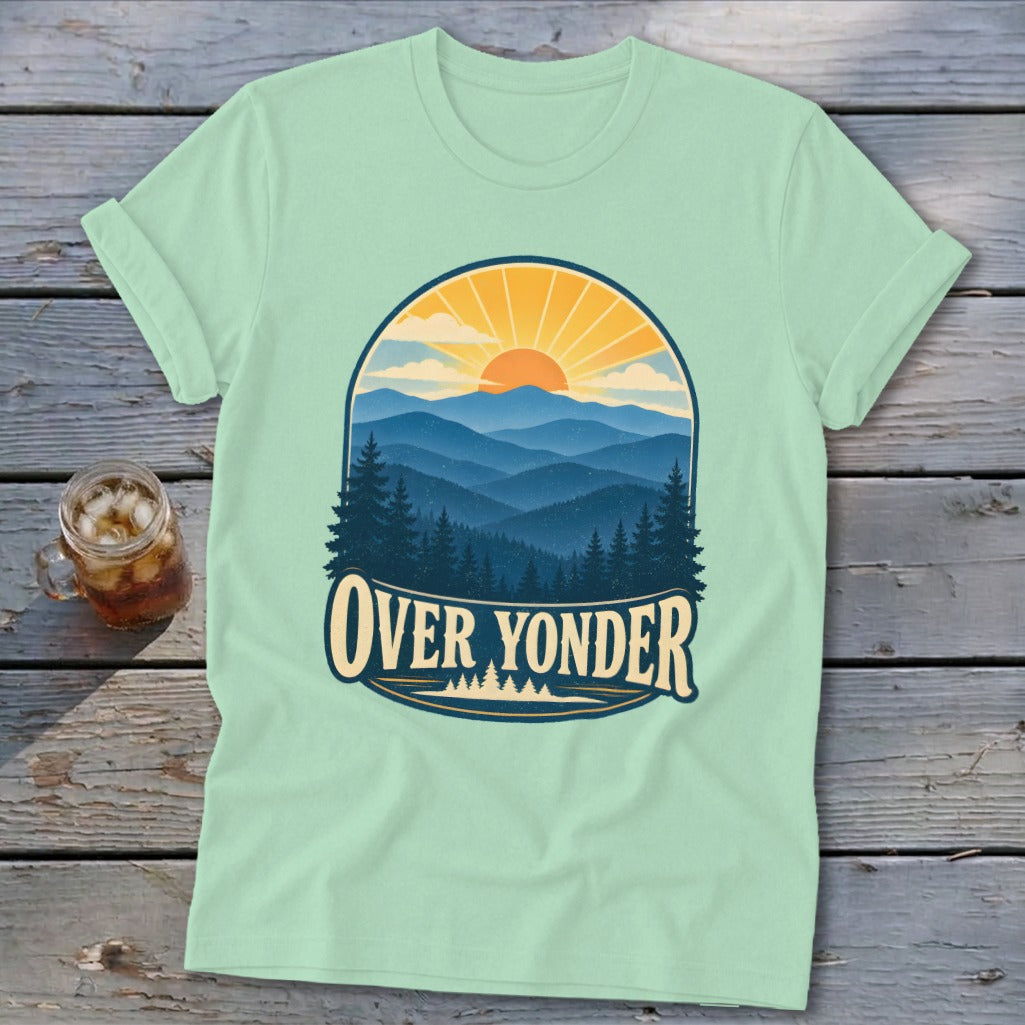 Light green t-shirt with a vintage mountain landscape graphic and the text Over Yonder on a wooden background.