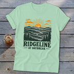 Mint t-shirt with a graphic of a sunrise over mountains and the text "RIDGELINE AT DAYBREAK".