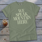 Olive green t-shirt with text "WE SPEAK MOUNTAIN HERE" and a glass of iced tea.