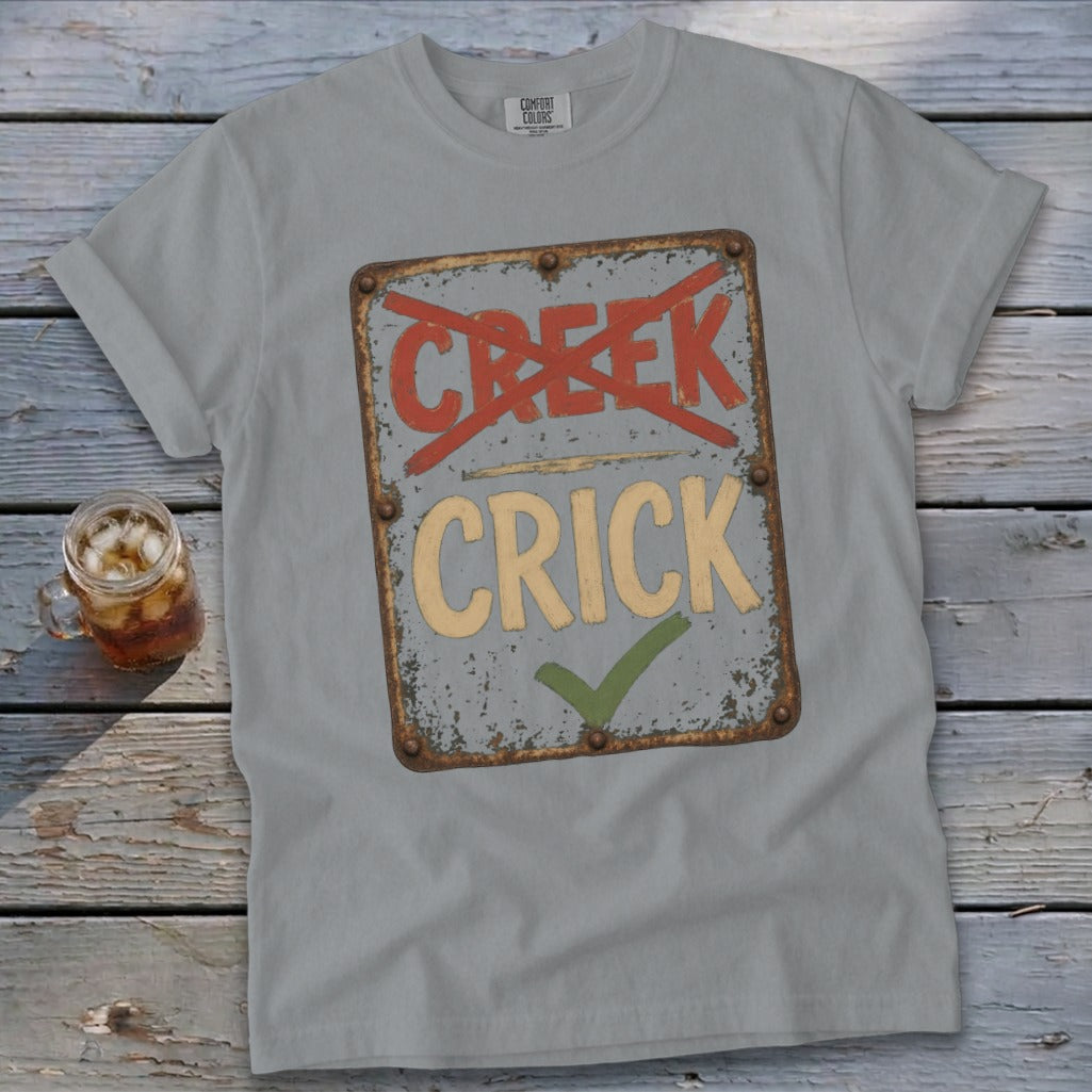 Gray t-shirt with a distressed sign graphic showing "CREEK" crossed out and "CRICK" with a checkmark.