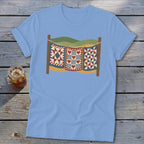Light blue t-shirt featuring a graphic of three patchwork quilts hanging on a clothesline outdoors.